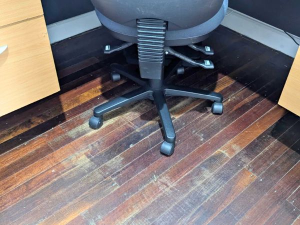 A damaged hardwood Jarrah floor with visible scratches and wear marks caused by an office chair without floor protection.